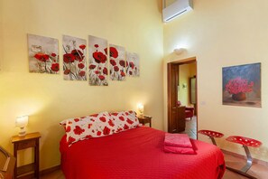 Un dormitorio con una cama, una mesita de noche, una lámpara, una silla y una puerta que da a otra habitación.