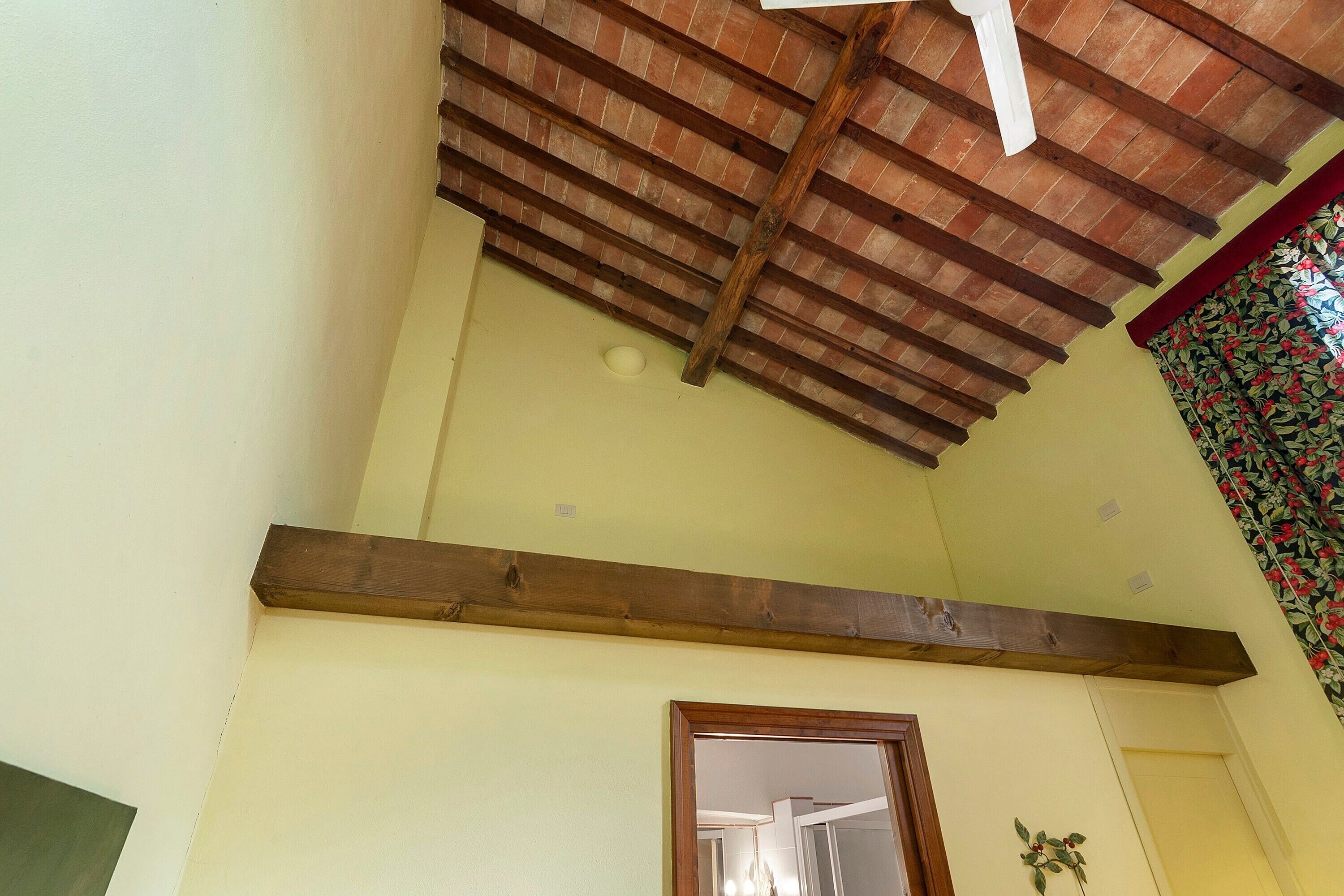 Um quarto com teto inclinado, uma viga de madeira, uma porta e parede com padrão floral.