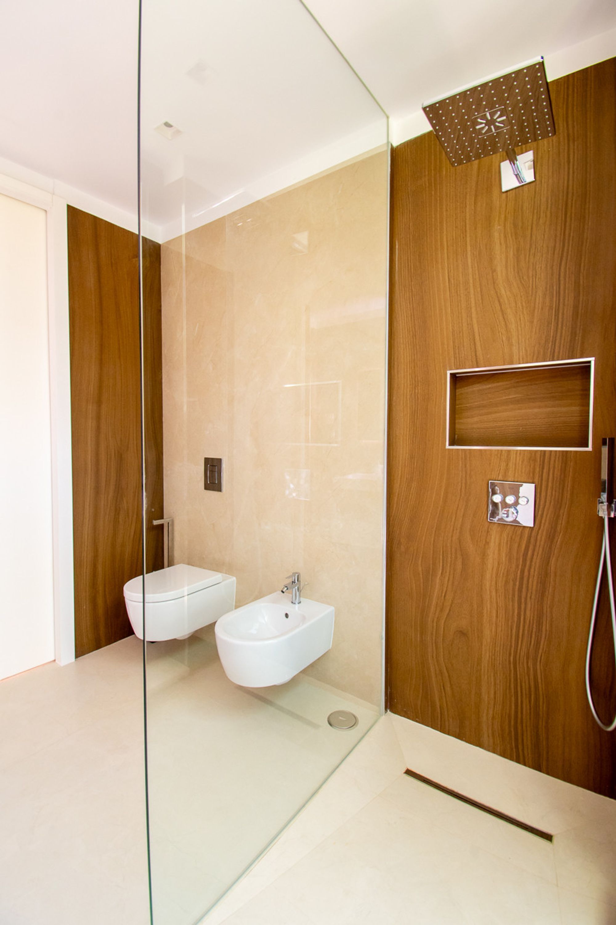 Et moderne badeværelse med glasafskærmning, en bidet, bruser og træpaneler.