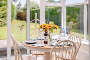 A dining table with plates, glasses, and a bottle of wine, set in a room with large windows and white chairs. - 2 Bed in Bridlington (oc-77607) (Sewerby)