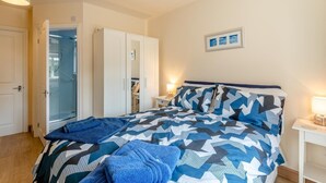 Een slaapkamer met een bed, een kledingkast, een badkamer met een glazen deur en een nachtkastje met een lamp.