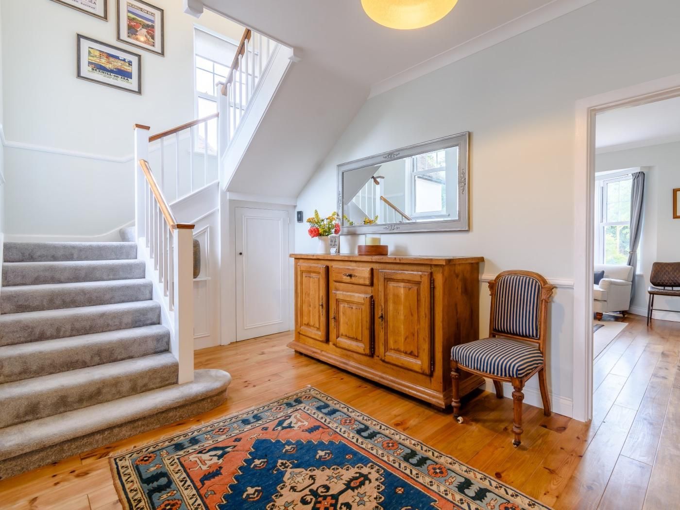 A staircase leading to a second floor, a wooden cabinet with drawers, a chair, and a patterned rug on a wooden floor.