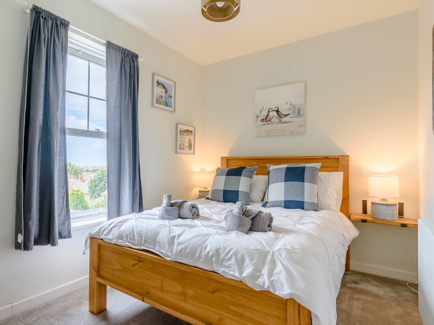 Une chambre à coucher avec un lit en bois, du linge de lit blanc, une fenêtre avec des rideaux et deux lampes de chevet.