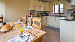 A kitchen with white cabinets, a dining table with breakfast items, and a window with a view of trees. - 2 Bed in Mold (oc-77603) (Pen-y-cefn)