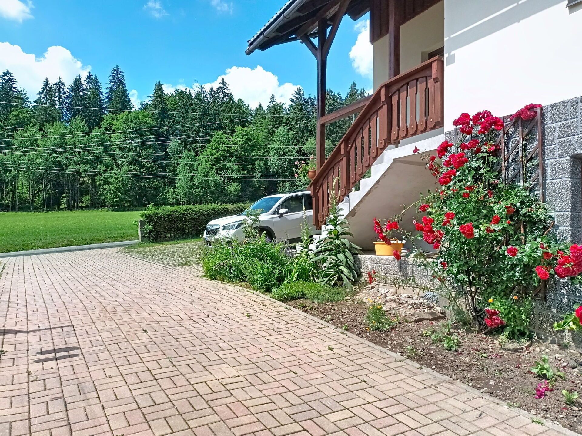 A paved driveway leading to a building with a wooden staircase and a car parked nearby.
