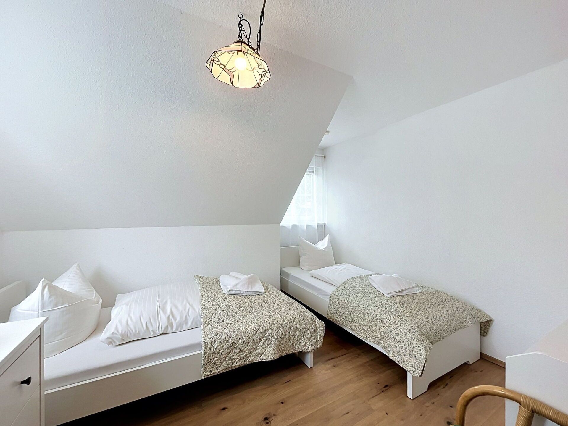 Une chambre avec deux lits, un luminaire suspendu et une fenêtre.