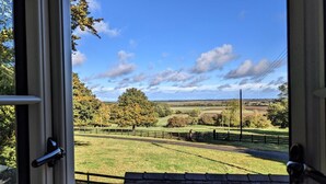 Blick durch ein offenes Fenster auf eine ländliche Landschaft mit Feldern, Bäumen und blauem Himmel.