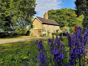 A stone building with a pitched roof, surrounded by lush greenery and purple flowers. - 2 Bed in Alford (oc-77637) (Rigsby)