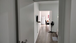 Ein Flur, der zu einer Küche mit Kühlschrank, einem Esstisch mit Stühlen und einem Standventilator führt.