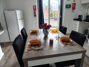 Ein Essbereich mit einem Tisch für vier Personen, einer Vase mit roten Blumen und Blick ins Freie durch ein Fenster.