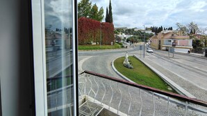 Blick aus einem Fenster auf eine Straße mit Kreisverkehr, einer Statue und einem Gebäude mit rotem Heckenrondell.