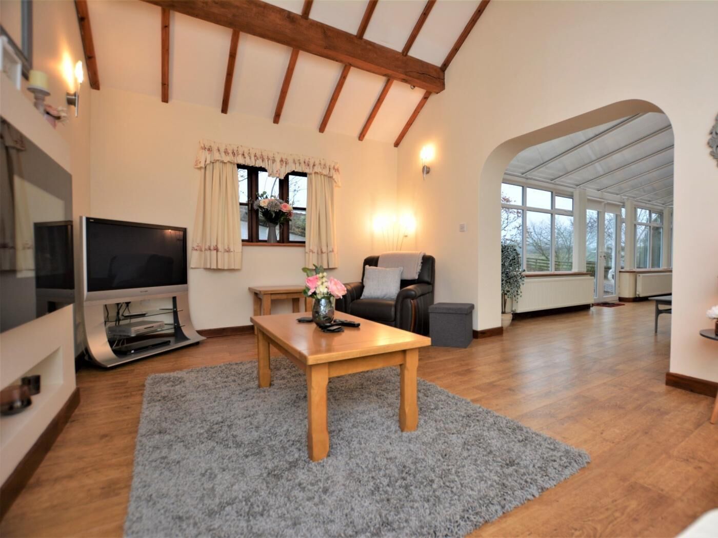 Una sala de estar con televisor, mesa de madera, sofá y ventana con cortinas.