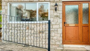 Une façade en pierre avec une porte en bois et une fenêtre ornée d’un garde-corps en métal.