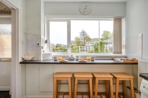 Eine Küche mit Fenster, Holzstühlen, einer Uhr und Frühstücksutensilien auf der Arbeitsfläche.