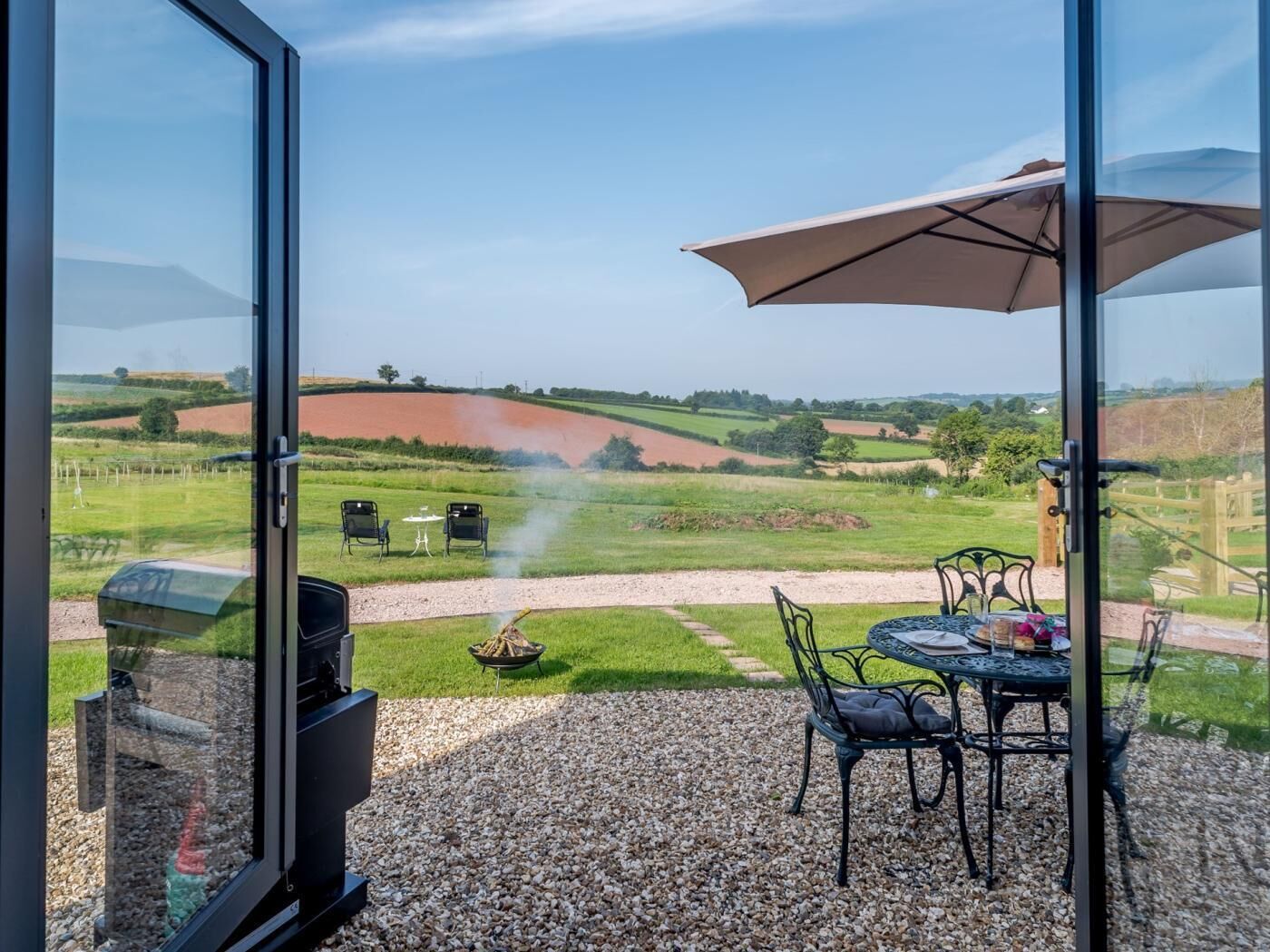 A patio with outdoor seating, a grill, and a view of a rural landscape.