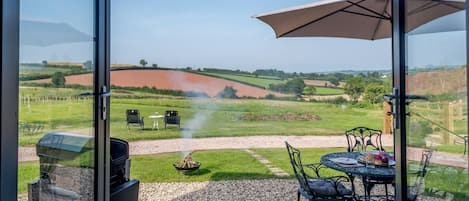 A patio with outdoor seating, a grill, and a view of a rural landscape.