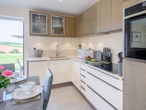 A modern kitchen with a built-in oven, a sink, and a dining area with a table set for two. - 2 Bed in Crediton (oc-78468) (Cheriton Fitzpaine)