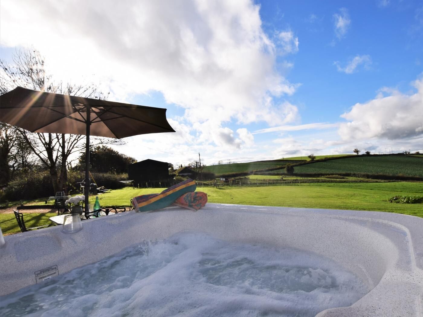 A hot tub with a view of rolling hills and a cloudy sky.