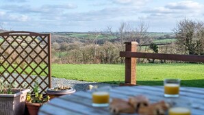 Eettafel met eten en drinken, een houten hek en uitzicht op een groen landschap.