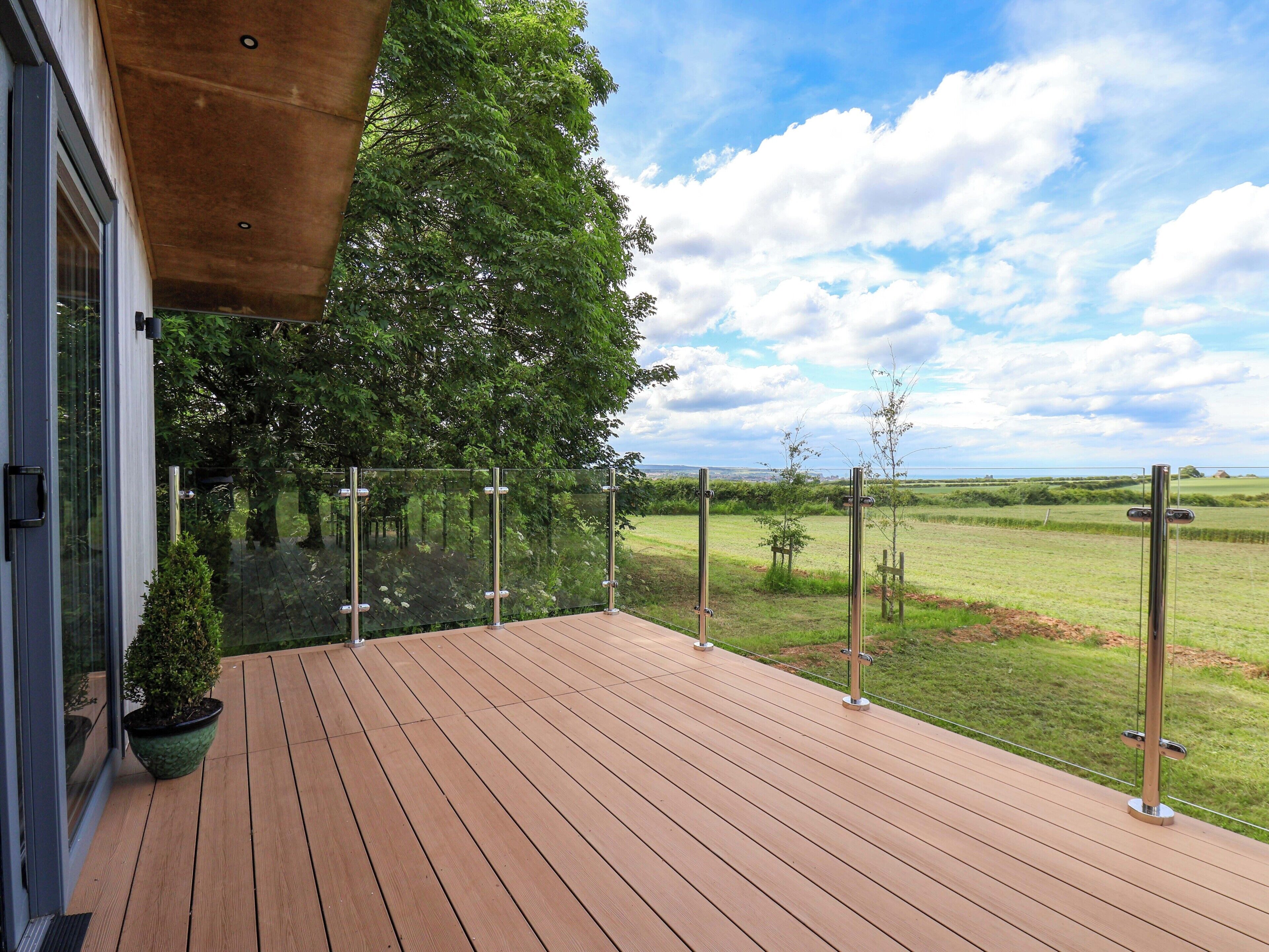 A wooden deck with a glass railing overlooking a grassy field and a clear sky.