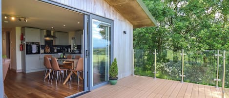A modern house with a wooden deck, a glass door leading to a dining area, and a view of greenery.