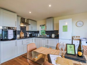 A modern kitchen with white cabinets, a built-in oven, and a dining area with a glass table and chairs. - Freedom Lodge @ Summerfield Farm (Whitby)