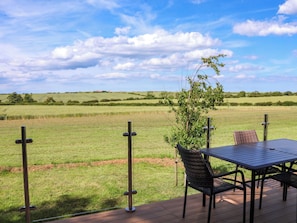 A deck with a table and chairs overlooking a grassy field. - Freedom Lodge @ Summerfield Farm (Whitby)