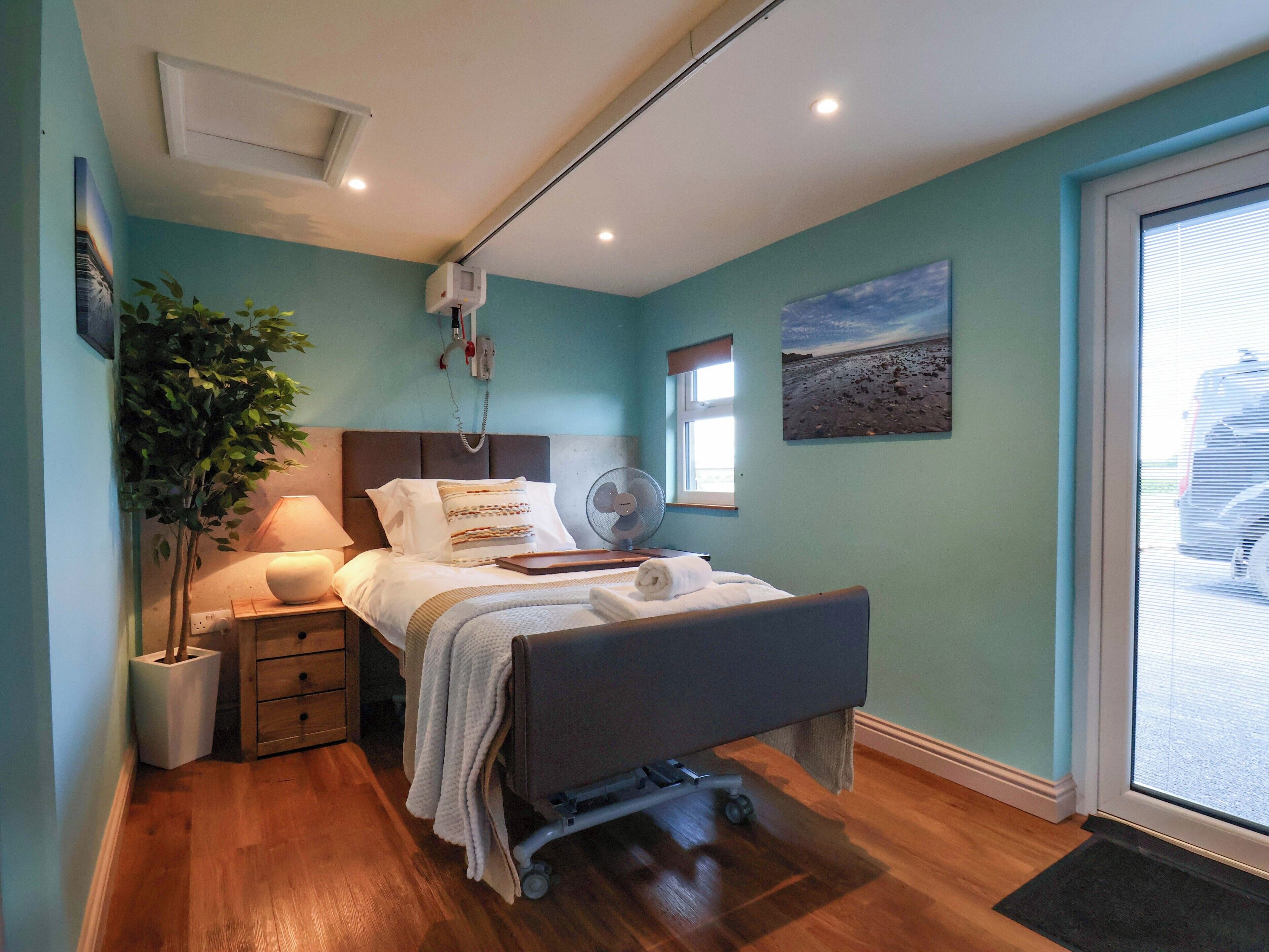 A bedroom with a bed, bedside table, lamp, and a large window.
