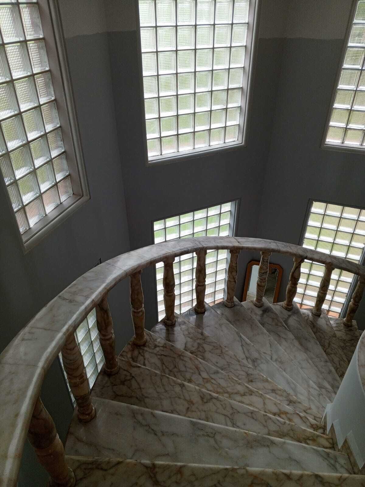 A marble staircase with a curved railing and multiple windows with metal grilles.