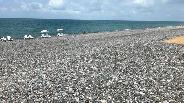 Una playa de guijarros con sillas de descanso y sombrillas.