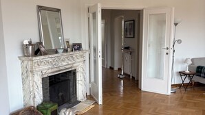 Un vaste salon agrémenté d’une cheminée en marbre, d’un grand miroir et d’un parquet en bois disposé en point de Hongrie.