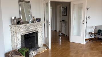 A spacious living room with a marble fireplace, a large mirror, and a herringbone wooden floor.