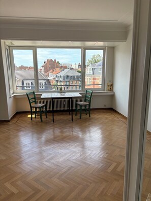 A room with a large window, a table with chairs, and a radiator. - Spacious 1-bedroom apartment in charming Uccle, with office and balcony (Uccle)