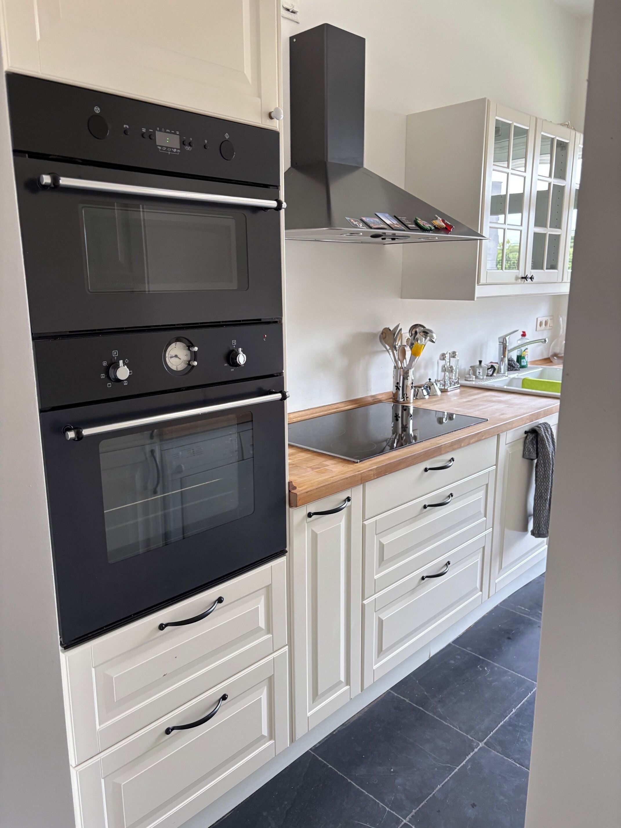 Eine Küche mit einem Kombi-Backofen, einer Spüle und weißen Schränken.