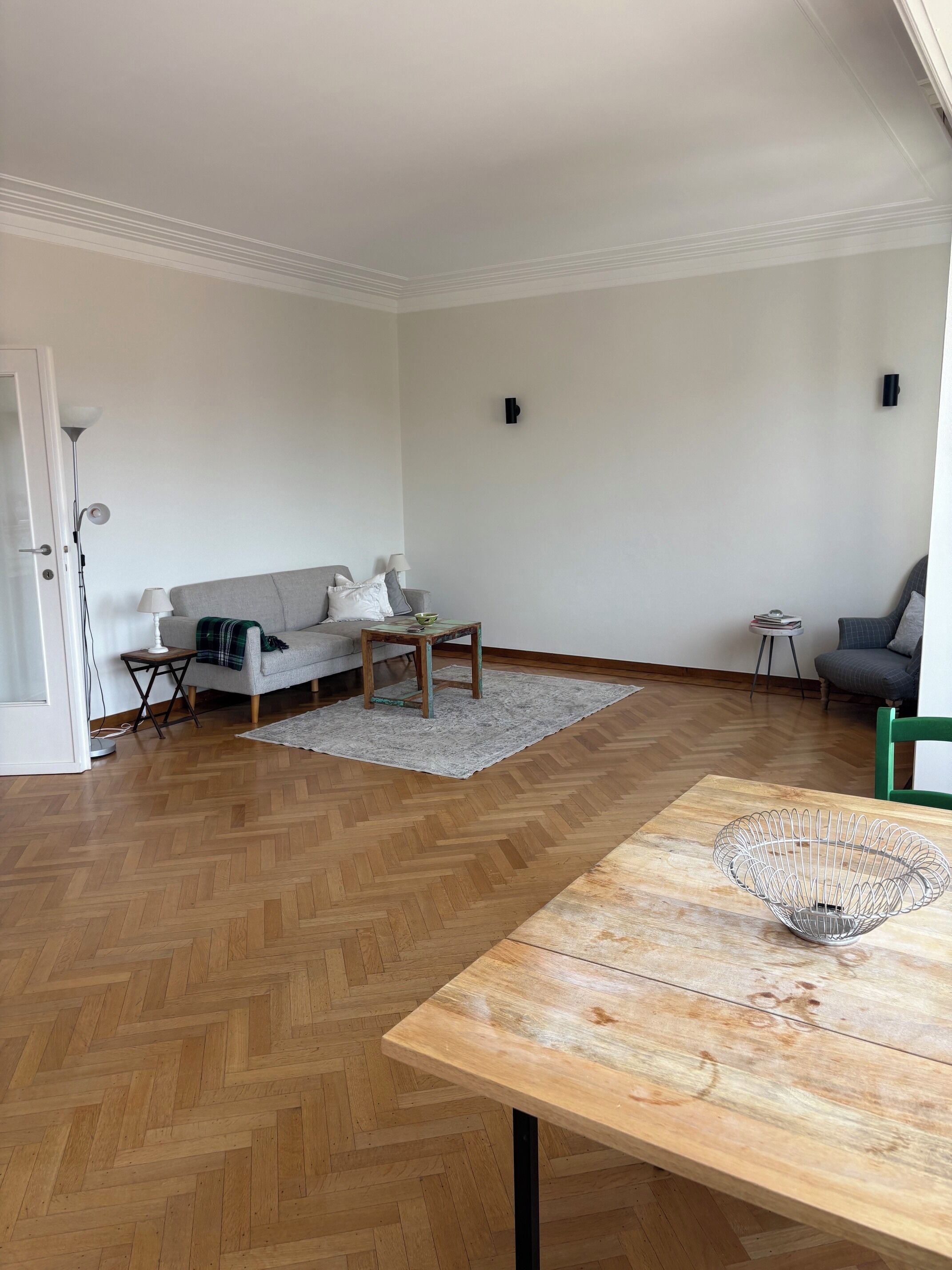 A modern living room with a herringbone floor, a wooden coffee table, a grey sofa, and a green chair.
