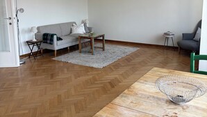 Un salon moderne avec un parquet en chevrons, une table basse en bois, un canapé gris et un fauteuil vert.