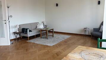 A modern living room with a herringbone floor, a wooden coffee table, a grey sofa, and a green chair.