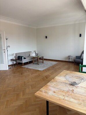 A modern living room with a herringbone floor, a wooden coffee table, a grey sofa, and a green chair.