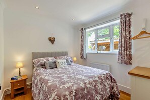 A bedroom with a bed, bedside lamps, a window with curtains, a radiator, and a wooden bedside table. - 2 Bed in Godshill (oc-78573) (Godshill)