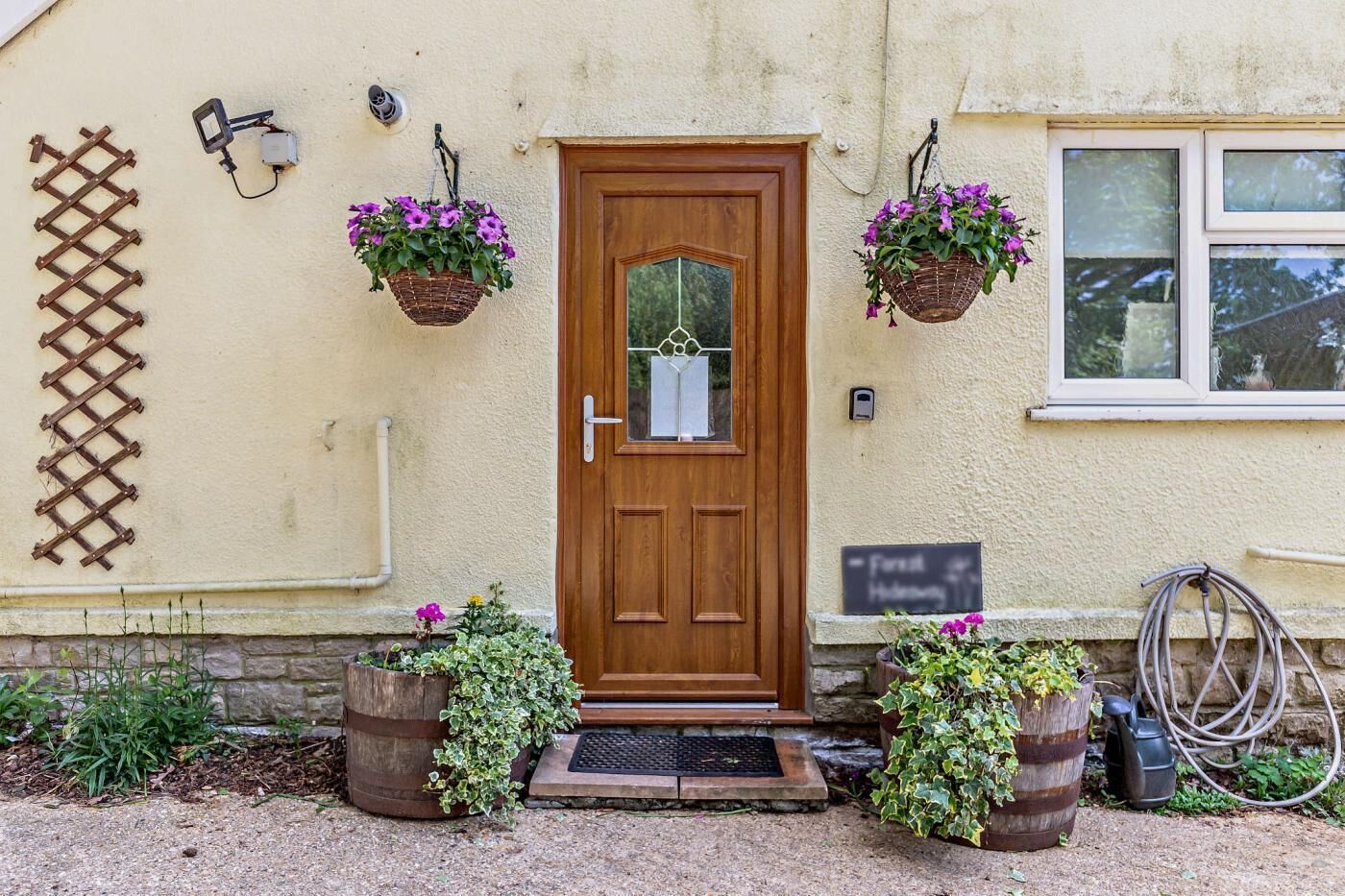 A wooden door with a window above, two hanging flower baskets, a metal gate, and a stone wall.