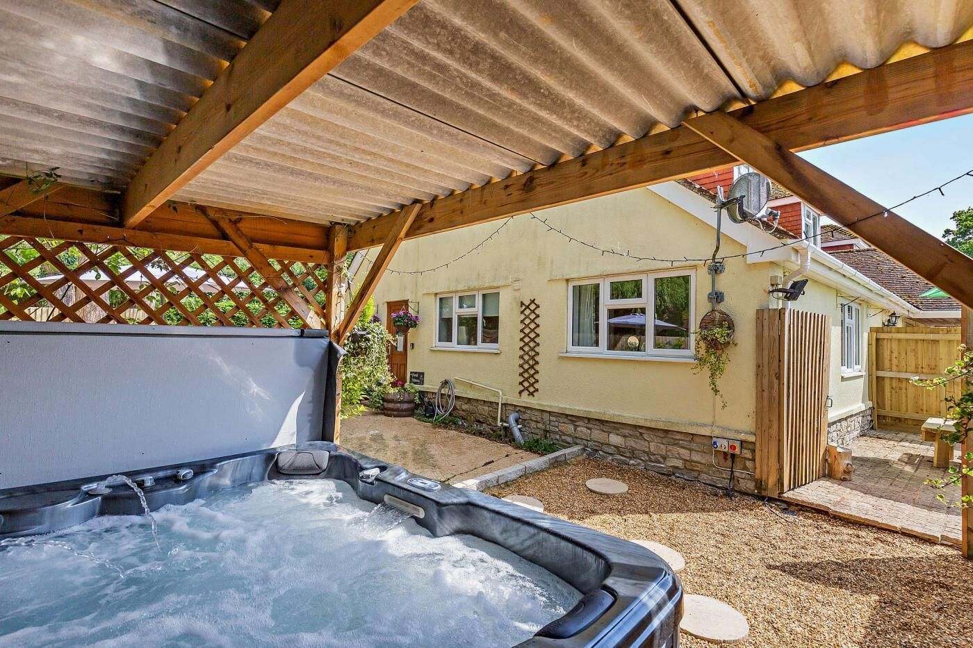 Et boblebad under et træbeklædt pergola med et hus i baggrunden.