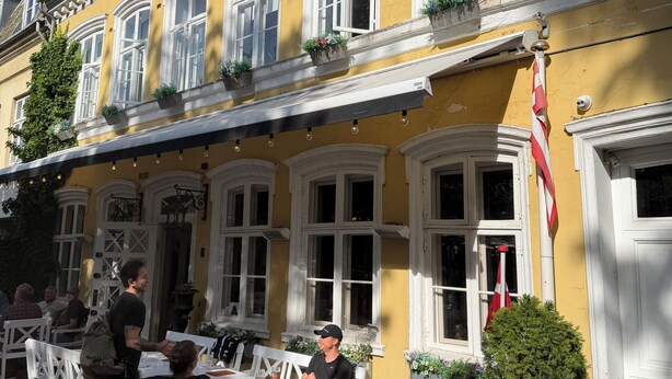 A yellow building with white windows and a flag, outdoor seating with tables and chairs, and potted plants on the balcony. - Hotel Allegade 10 (Frederiksberg)