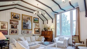 A room with a high ceiling, wooden beams, a fireplace, a sofa, a coffee table, and a large window with curtains. - 5 Bed in Inverness (oc-78538) (Drumnadrochit)