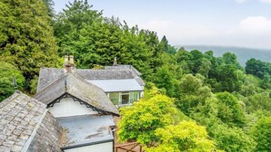 A house with a sloped roof, surrounded by lush greenery and trees. - 5 Bed in Inverness (oc-78538) (Drumnadrochit)