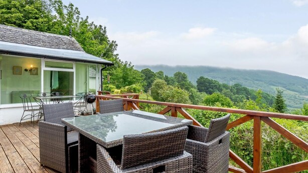 A deck with wicker furniture and a glass table overlooking a forested valley. - 5 Bed in Inverness (oc-78538) (Drumnadrochit)