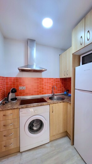 A compact kitchen with a washing machine, a sink, and a stove. - Sol Suites Apartment with a Balcony (Fuengirola)