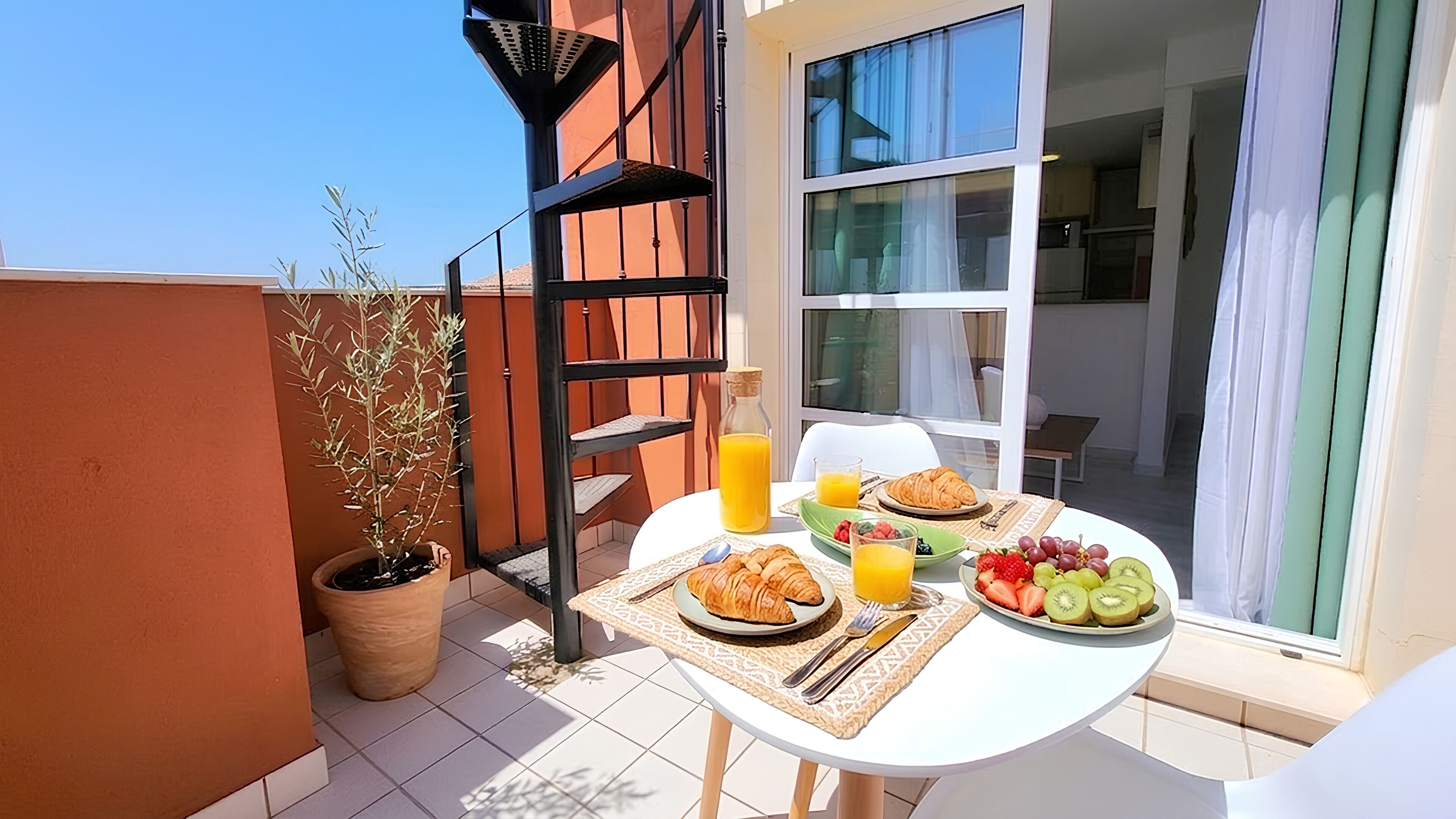A balcony with a table set for breakfast, including croissants, fruit, and orange juice.