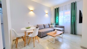 A modern living room with a sofa, a dining table with chairs, a coffee table, and a TV mounted on the wall. - Sol Suites Apartment with a Balcony (Fuengirola)