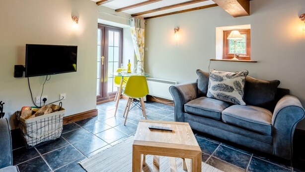 A living room with a sofa, a coffee table, a TV mounted on the wall, and a dining area with a table and chairs. - 1 Bed in Llangollen (oc-78471) (Glyn Ceiriog)