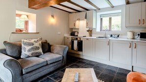A modern kitchen with white cabinets, a wooden ceiling, and a dining area with a grey sofa and a remote control on a table. - 1 Bed in Llangollen (oc-78471) (Glyn Ceiriog)
